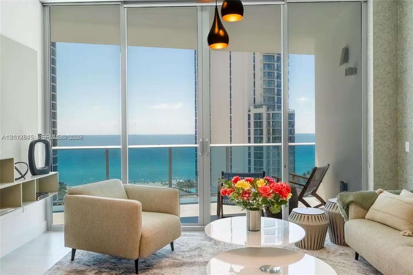 Floor-to-ceiling glass sliding doors, private balcony with metal railing, pendant light fixture with tiered shades, and custom built-in shelving