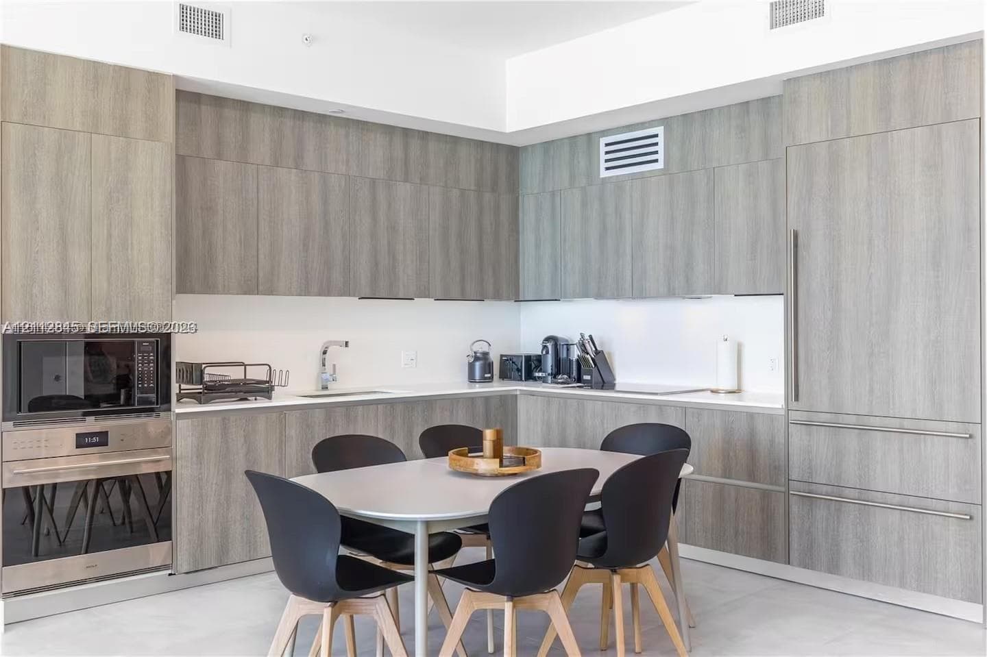Kitchen featuring flat-panel wood-finish cabinetry, integrated refrigerator, built-in stainless steel microwave and wall oven, and light-toned solid surface countertops