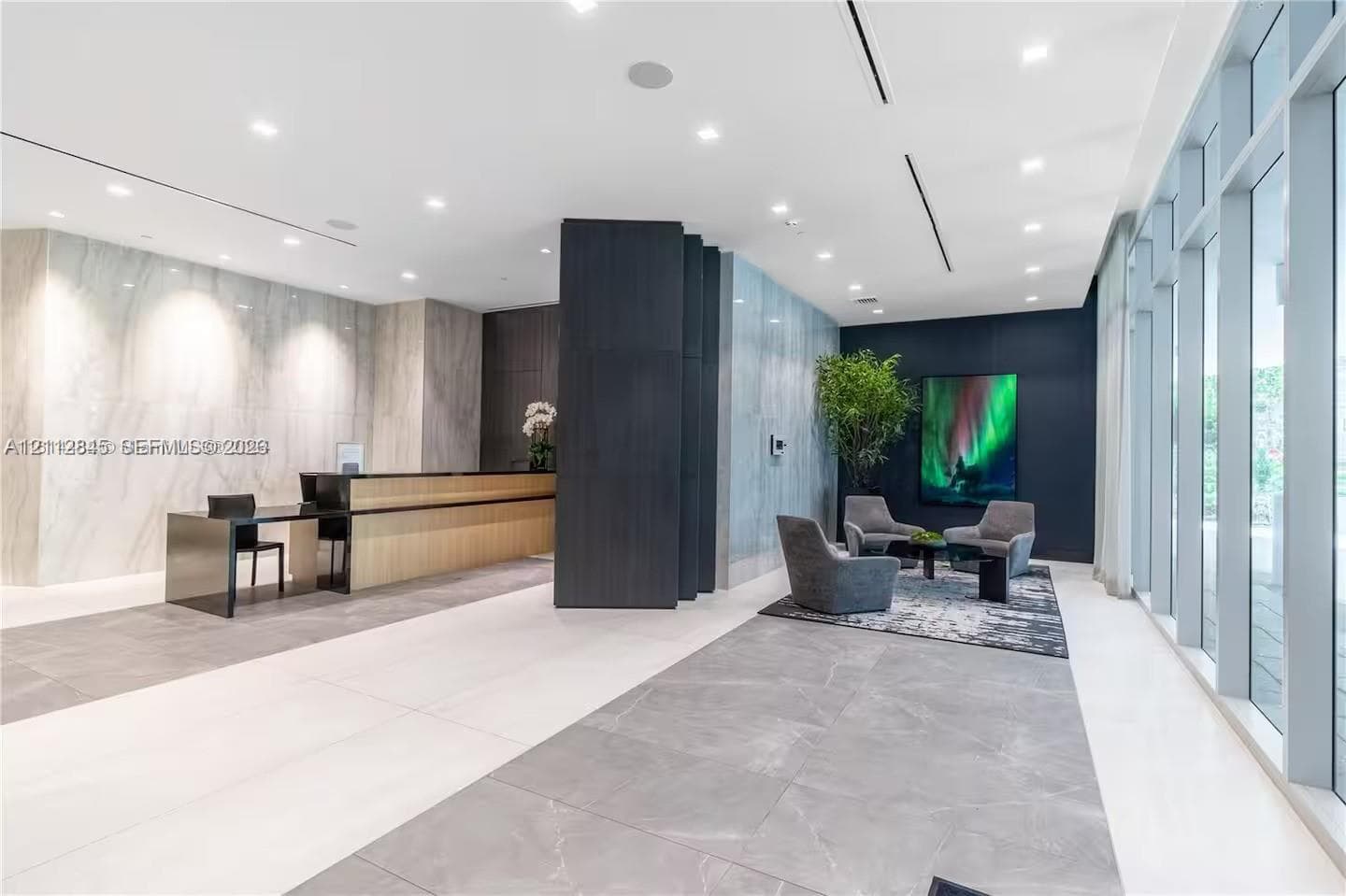 Lobby area featuring large-format tile flooring, stone-clad accent walls, floor-to-ceiling windows, recessed lighting, and a custom built-in reception desk
