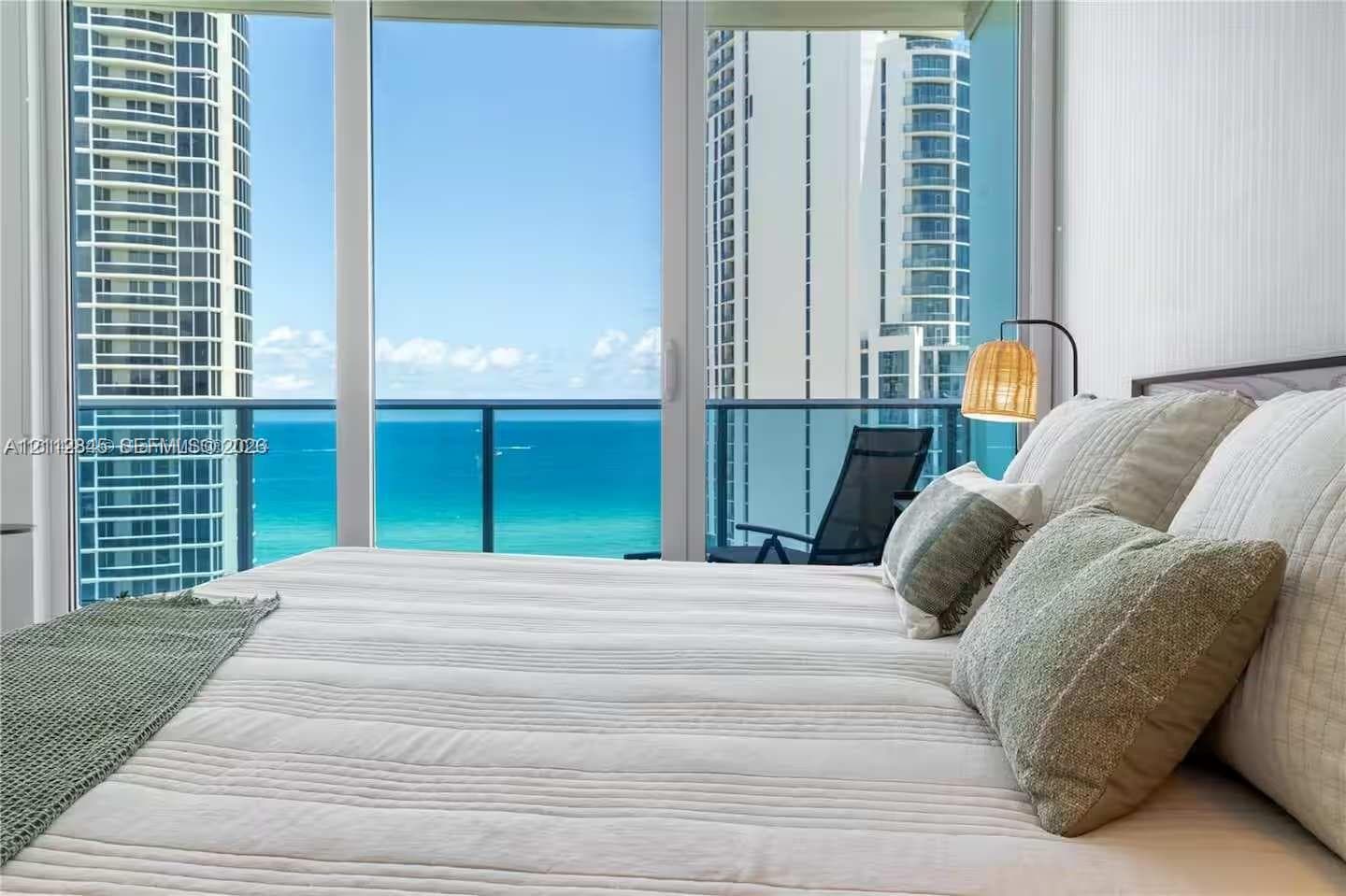 Floor-to-ceiling glass paneling featuring ocean and high-rise cityscape backdrops, with access to a private balcony enclosed by glass and metal railing