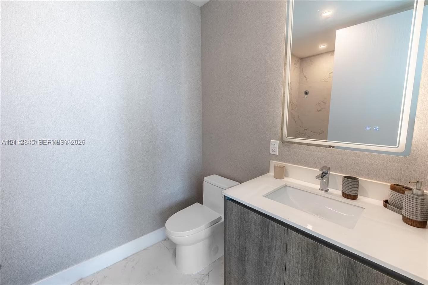 Modern vanity featuring a charcoal-finish cabinet, rectangular basin, and stone-surface countertop, complemented by a large integrated backlit mirror and white tile flooring