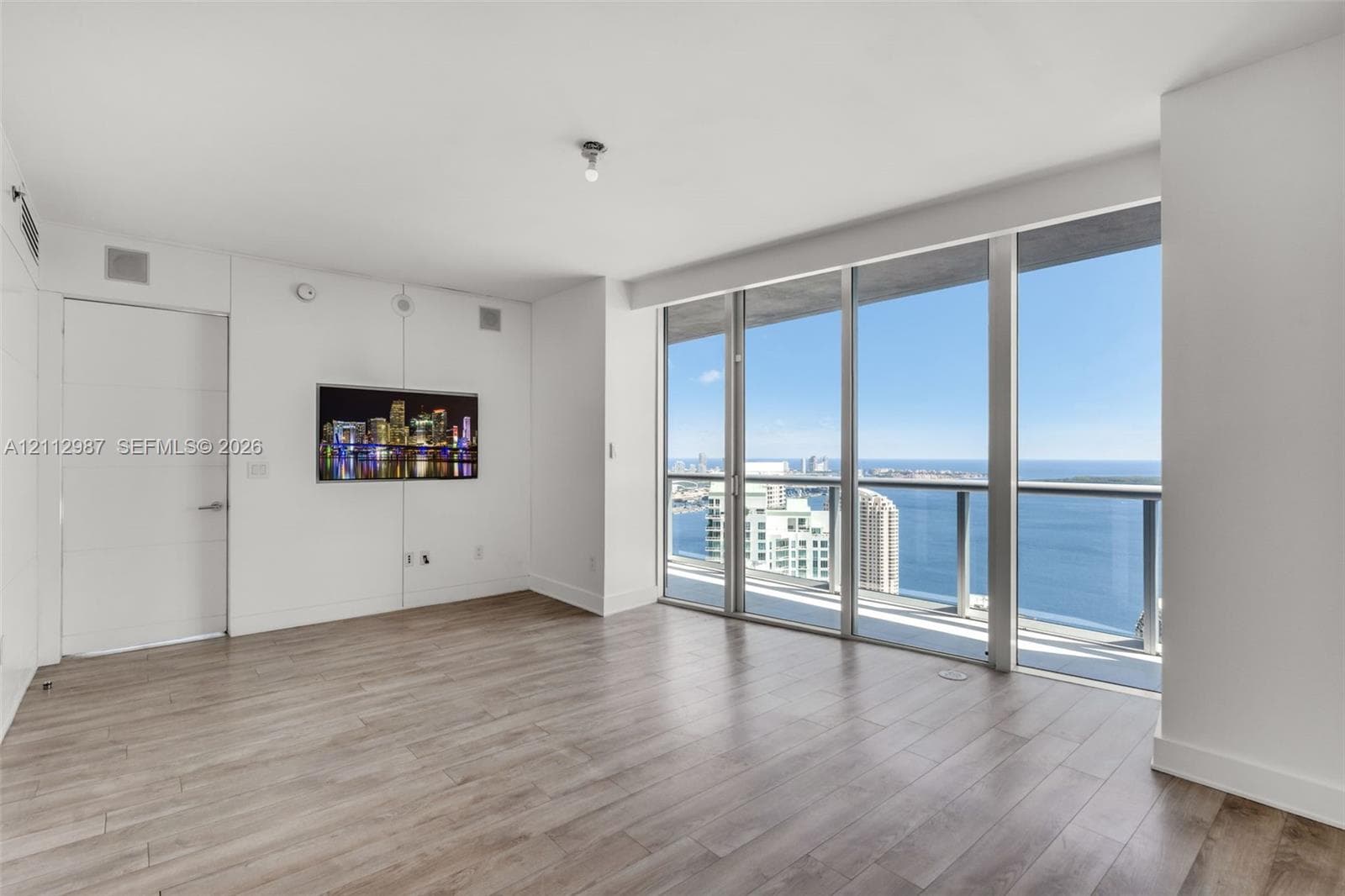 Floor-to-ceiling windows, private glass-railed balcony, wood-finish flooring, and minimalist white walls