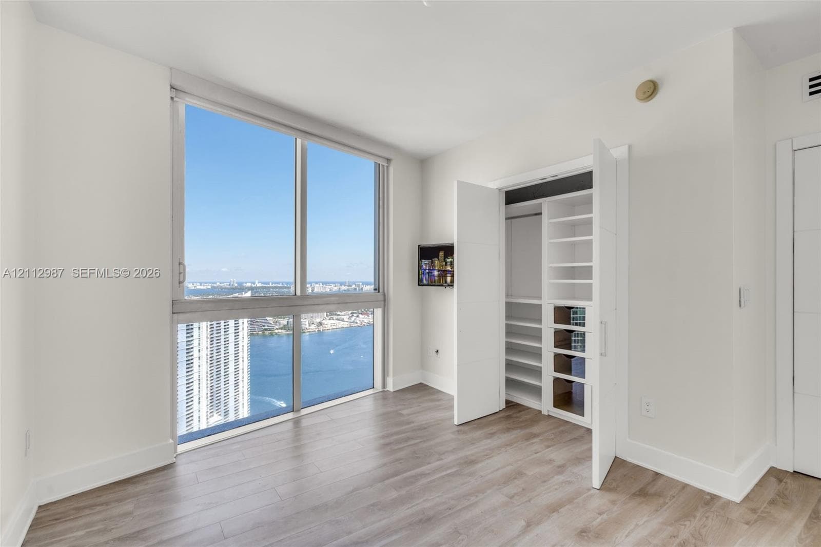 Floor-to-ceiling windows featuring expansive coastal scenery, wood-finish flooring, and built-in closet organization with shelving