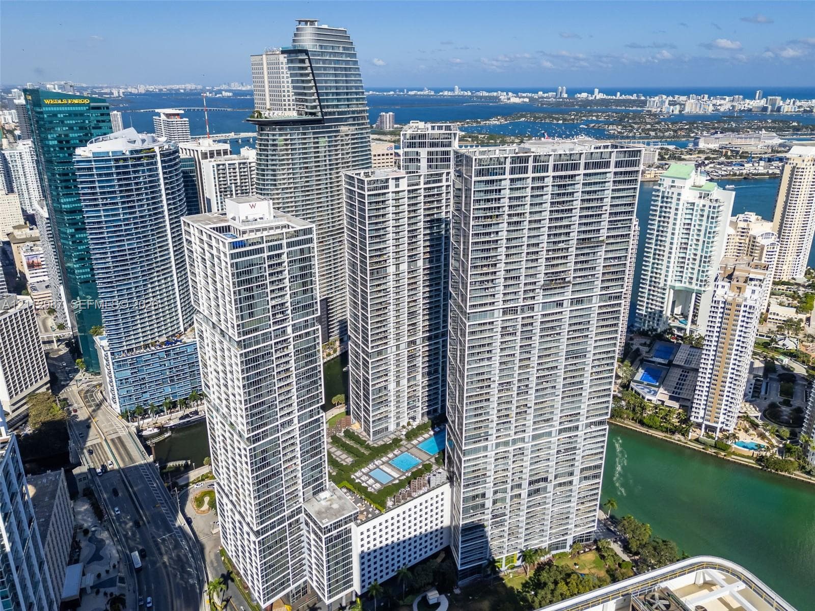 Aerial perspective of high-rise towers featuring glass-paneled facades, multiple swimming pools, and coastal water access