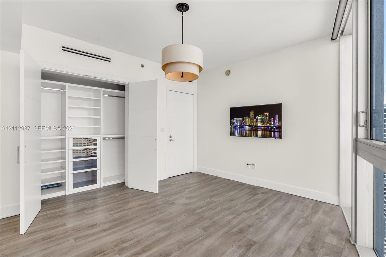 Wood-finish flooring, custom built-in closet system with integrated shelving and drawers, tiered drum pendant lighting, and floor-to-ceiling glass paneling