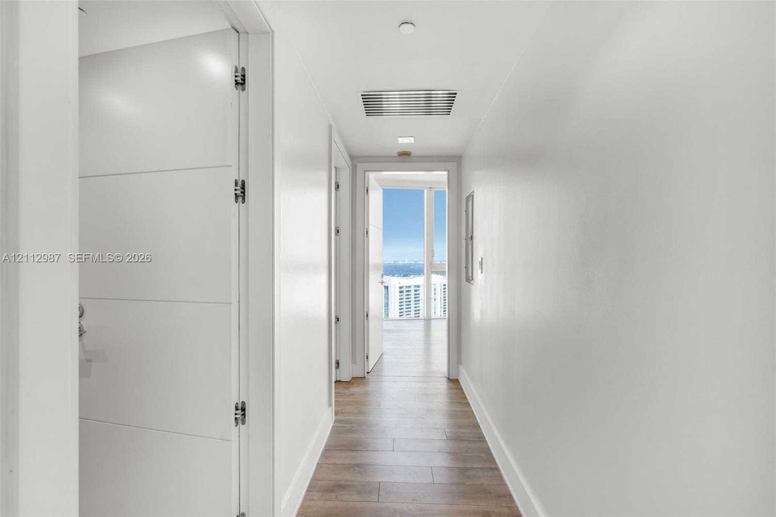 Hallway featuring horizontal-panel interior doors, light wood-finish flooring, and floor-to-ceiling windows with coastal scenery