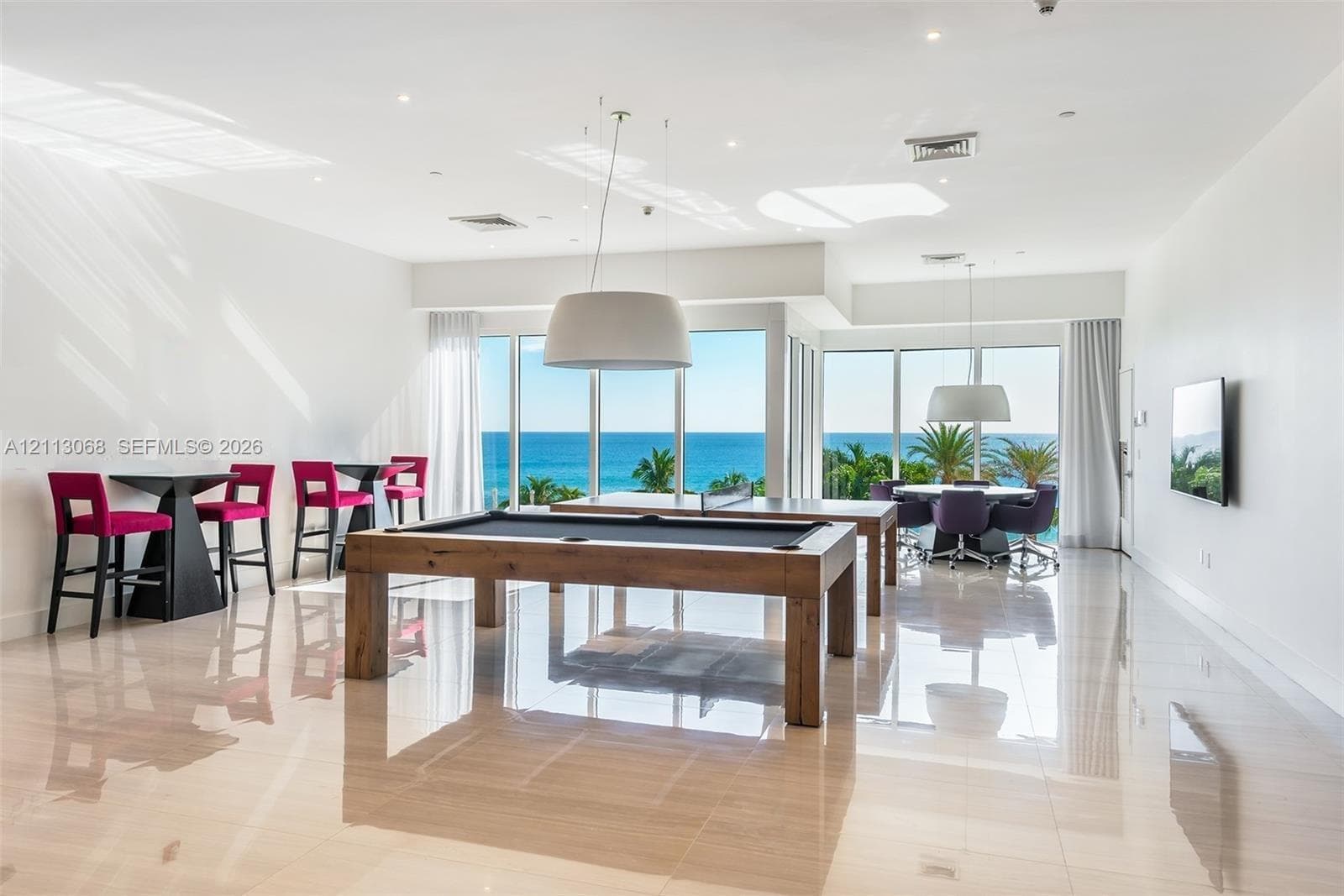 Spacious recreation area featuring large-format polished tile flooring, floor-to-ceiling windows, recessed lighting, and oversized drum pendant fixtures