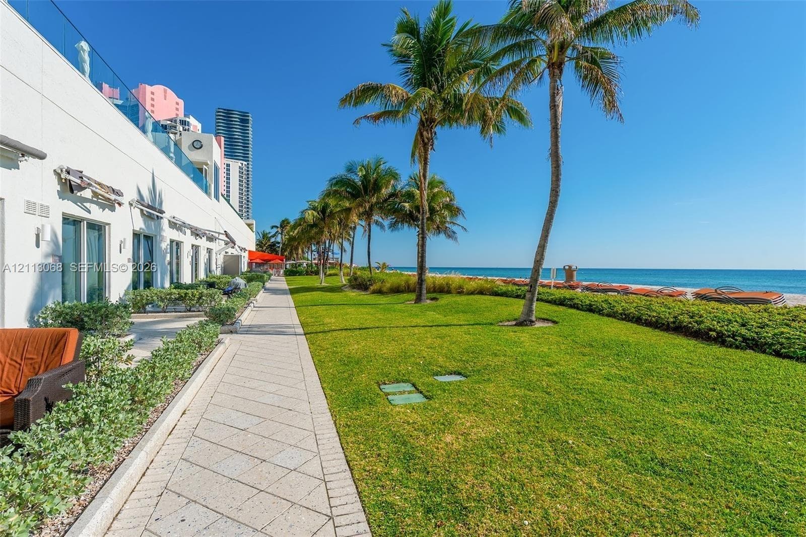 Expansive coastal lawn featuring mature palm trees, professional hardscaping, and direct oceanfront access