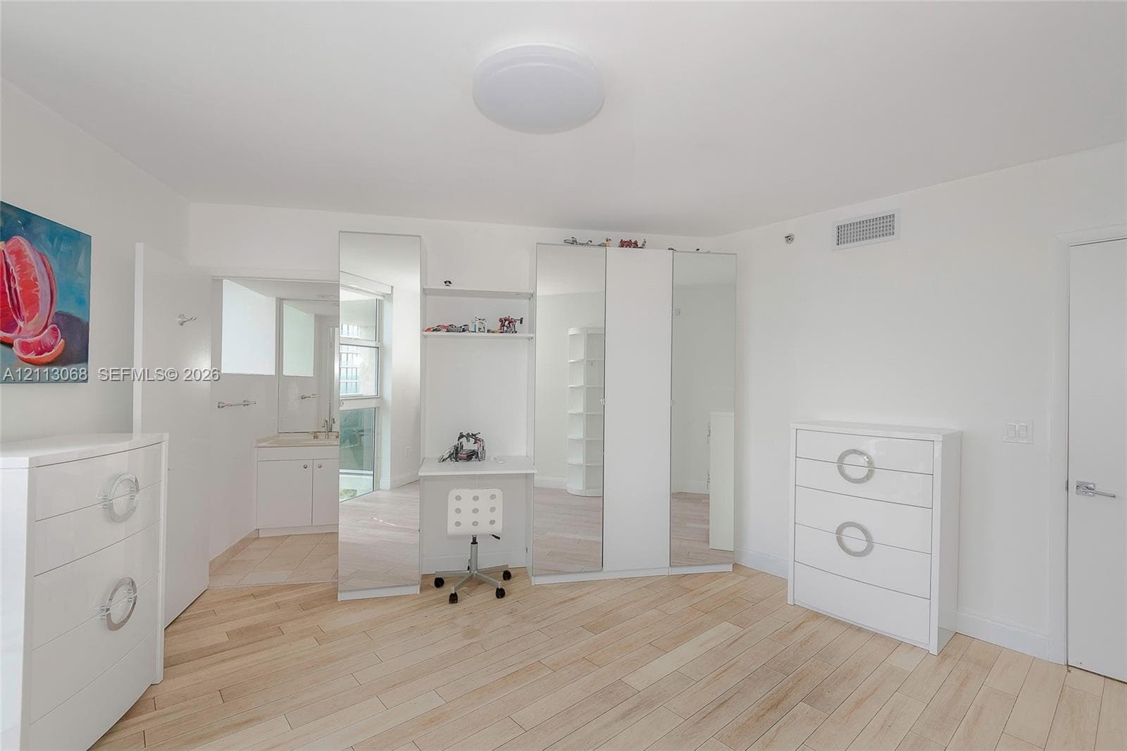 Wood-finish flooring, floor-to-ceiling mirror-faced closet cabinetry, and built-in desk workstation with overhead shelving