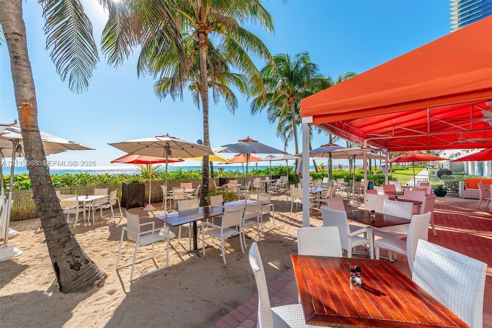 Outdoor terrace featuring a sand-surfaced dining area, brick-paver flooring, a permanent overhead metal awning, and native palm trees