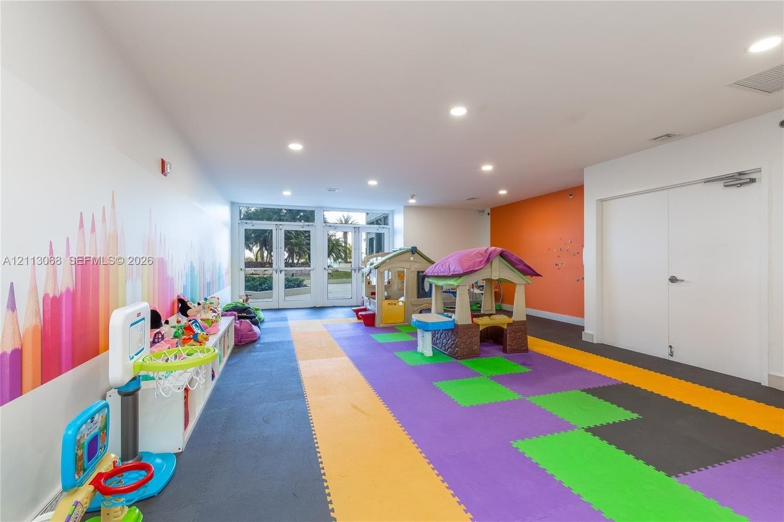 Open-plan interior space featuring recessed ceiling lighting, dual glass-paneled entry doors, and a decorative mural wall