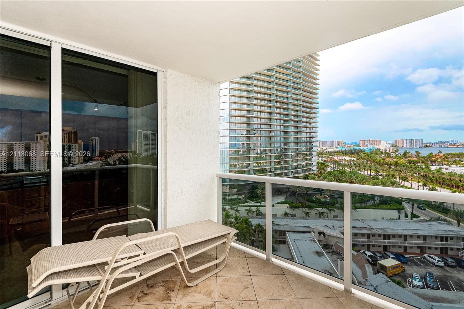 Covered balcony featuring stone-finish tile flooring, glass panel railings, and floor-to-ceiling sliding glass doors
