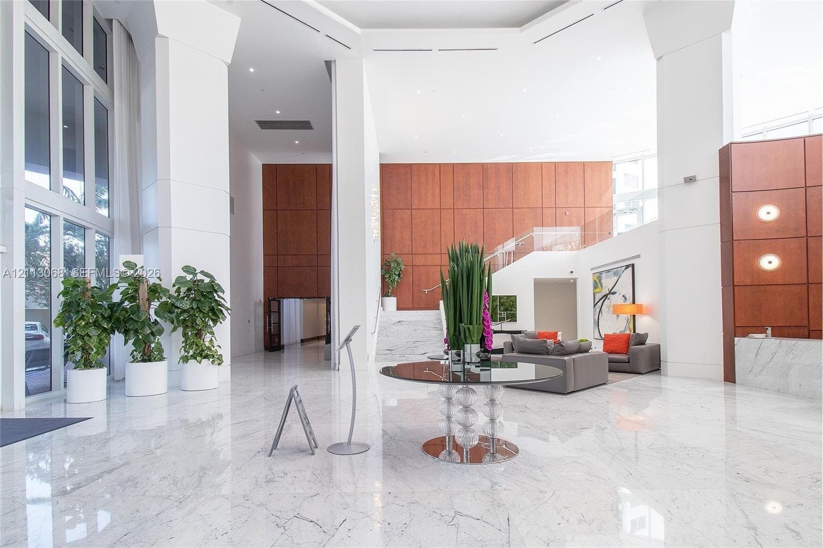 Grand lobby featuring soaring ceilings, polished stone flooring, extensive wood-paneled walls, floor-to-ceiling glass windows, and a glass-railed staircase