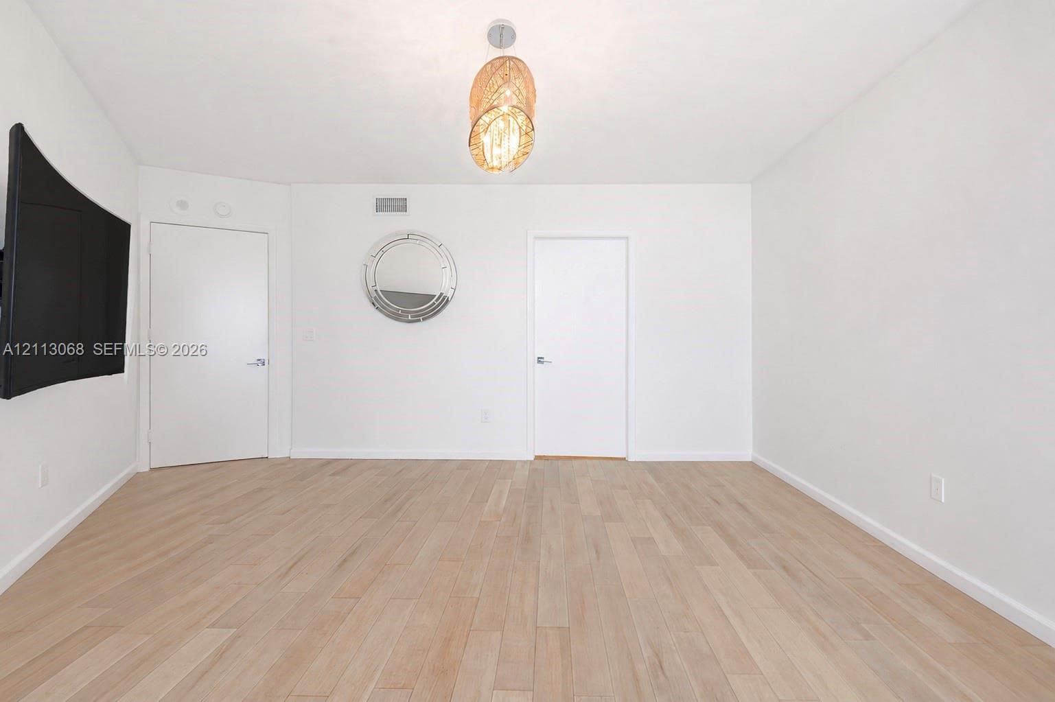 Light-toned wood-finish flooring, neutral walls, decorative pendant light fixture, and circular wall-mounted mirror
