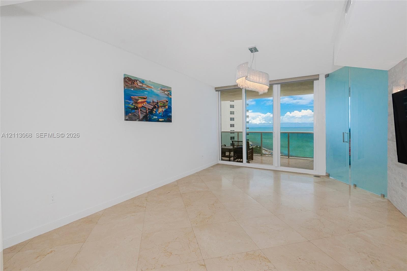 Open-concept space featuring polished stone flooring, floor-to-ceiling glass balcony doors, custom translucent glass partition, and contemporary chandelier lighting