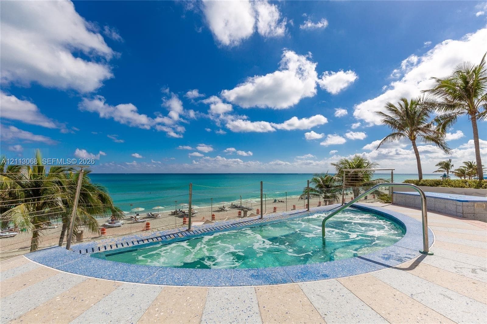 Elevated hot tub featuring a blue tile surround, stainless steel handrail, and a stone-paver deck