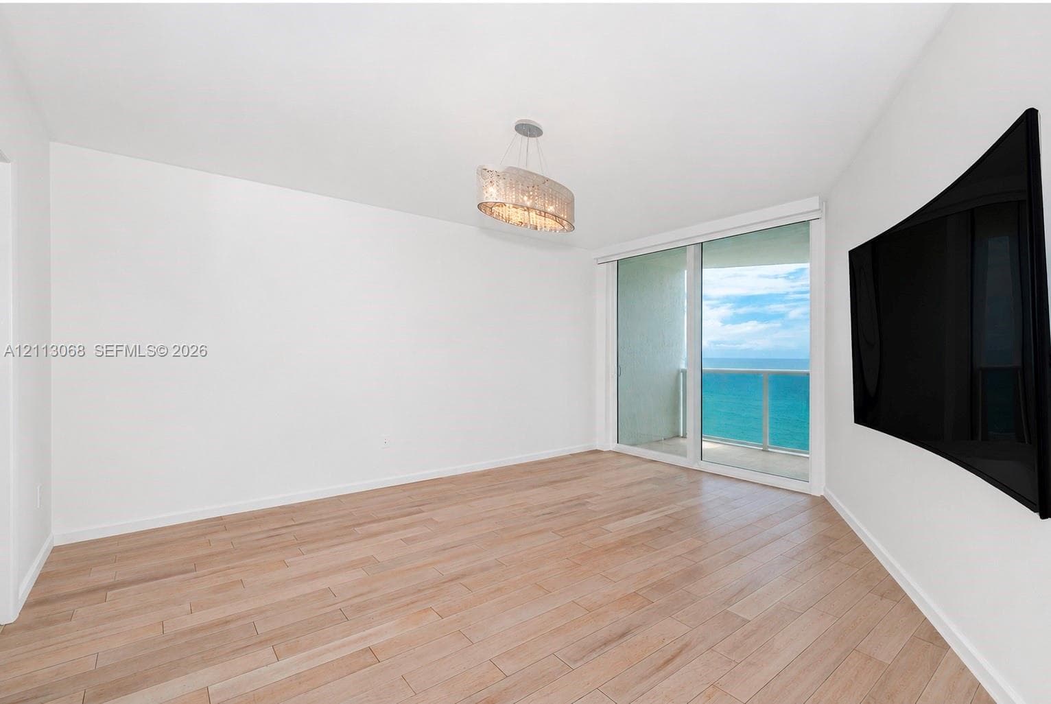 Interior space featuring wood-finish flooring, a tiered drum pendant light fixture, and a large sliding glass door opening to a balcony with water scenery