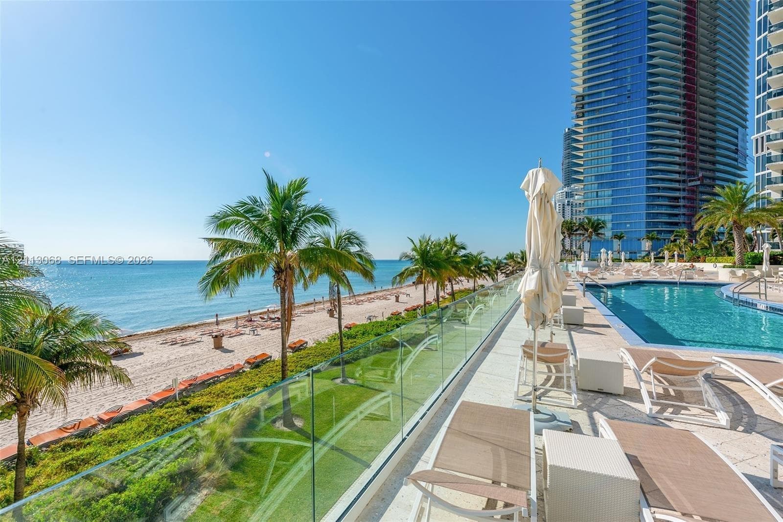 Outdoor swimming pool featuring a glass balustrade, paved deck, and surrounding palm trees with direct oceanfront access