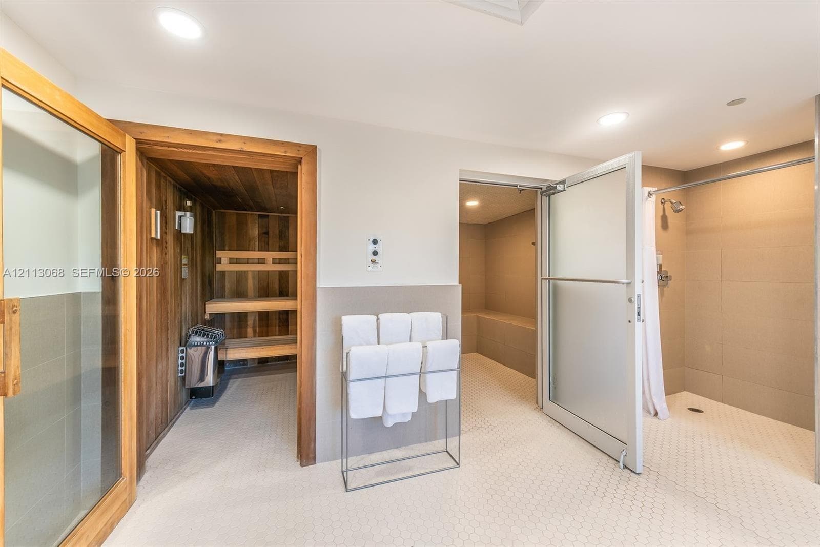 Sauna featuring wood-lined walls and built-in benches, steam room with tiled interior, and walk-in shower with large-format wall tiles and a glass door