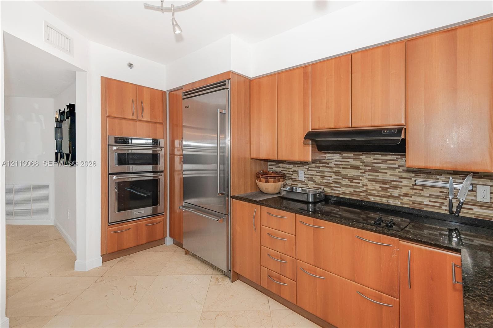 Kitchen featuring natural wood-finish cabinetry, stone countertops, stainless steel appliances, built-in double wall ovens, and tile flooring