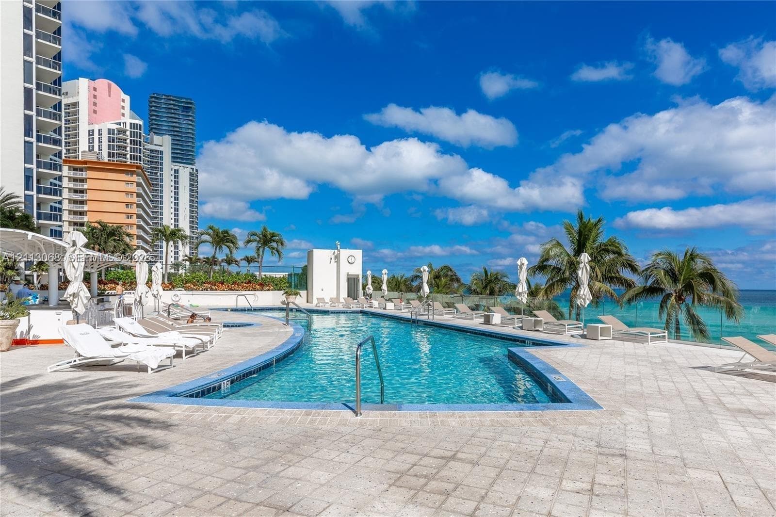 Outdoor swimming pool featuring a tiled surround, glass perimeter fencing, and palm tree landscaping