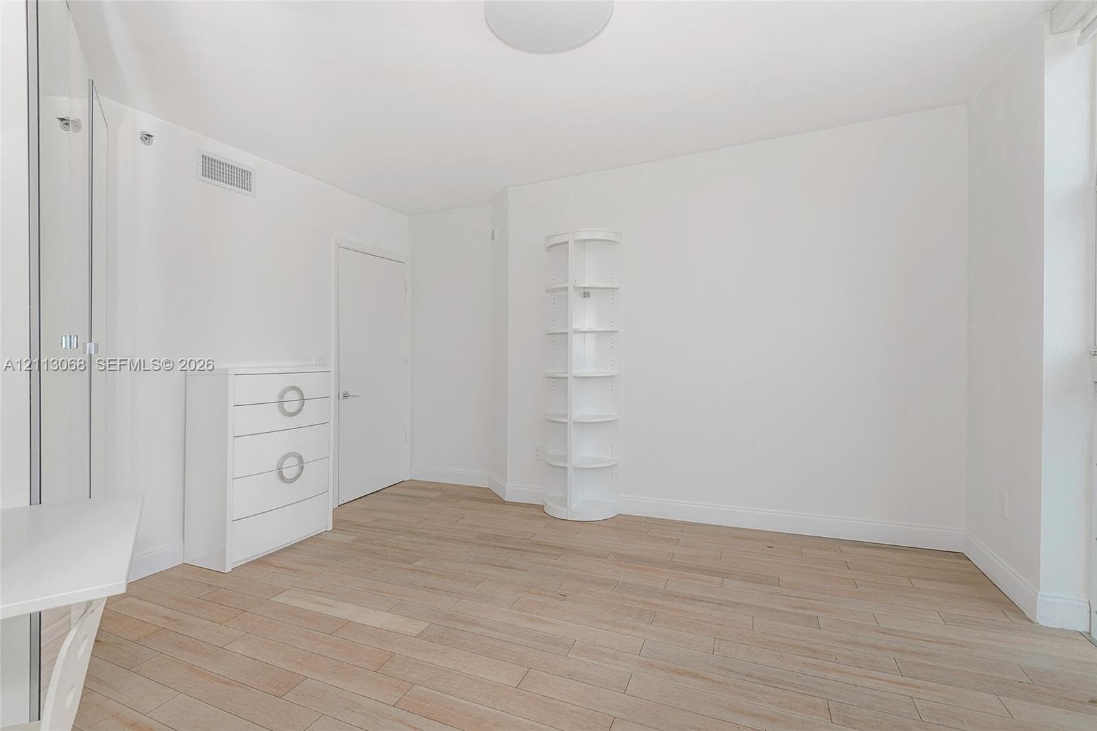 Neutral-toned interior featuring wood-finish flooring, white walls, and a built-in corner display shelving unit