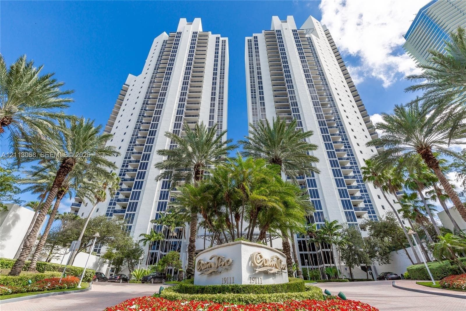 High-rise residential towers featuring glass balconies, reinforced concrete exterior, and manicured tropical landscaping with ornamental floral beds