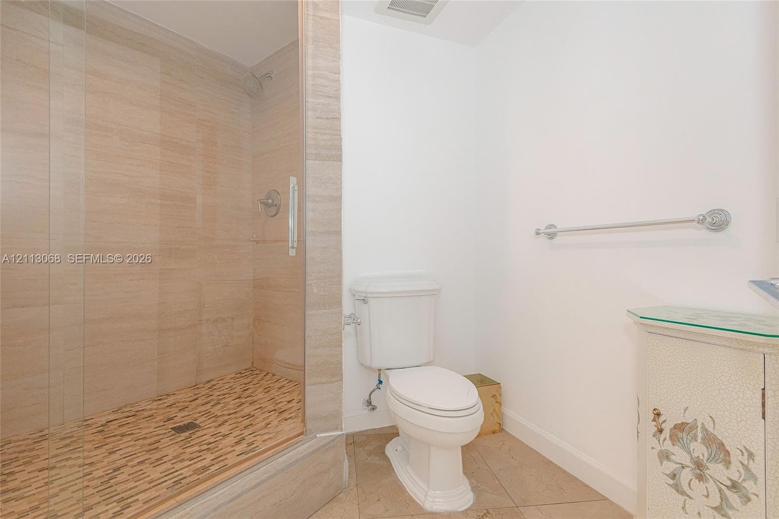 Walk-in shower with floor-to-ceiling neutral tile surround, glass enclosure, mosaic-tile shower pan, chrome fixtures, and ceramic tile flooring