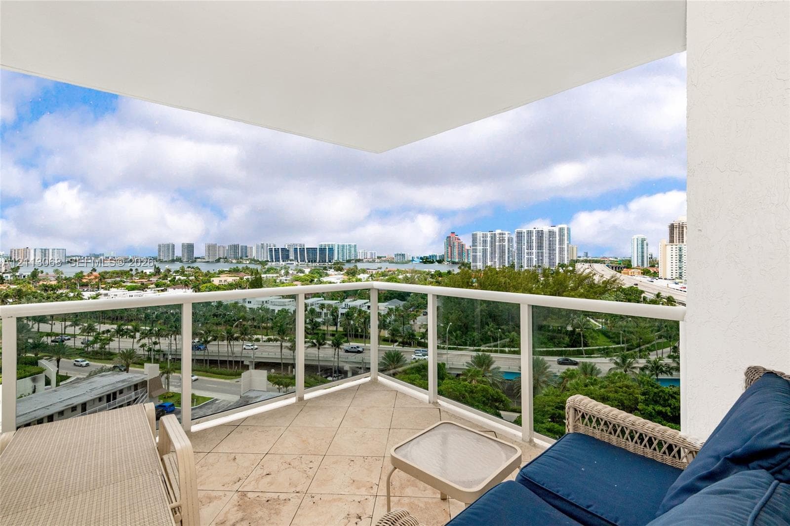 Covered balcony featuring oversized stone-look tile flooring and glass panel railings with metal framing
