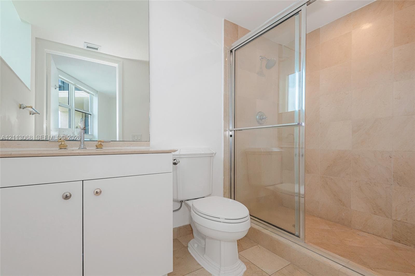 Bathroom featuring white cabinetry, a neutral stone-look countertop, a large wall-mounted mirror, and a walk-in shower with floor-to-ceiling tile surround and glass enclosure
