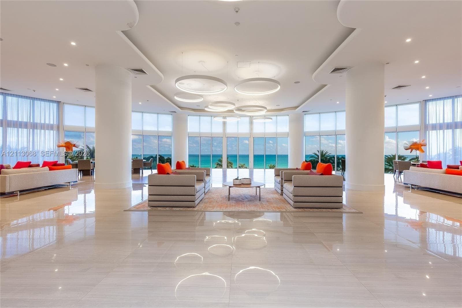 Open-concept space featuring floor-to-ceiling windows, polished stone flooring, recessed tray ceiling detailing, and custom circular pendant lighting