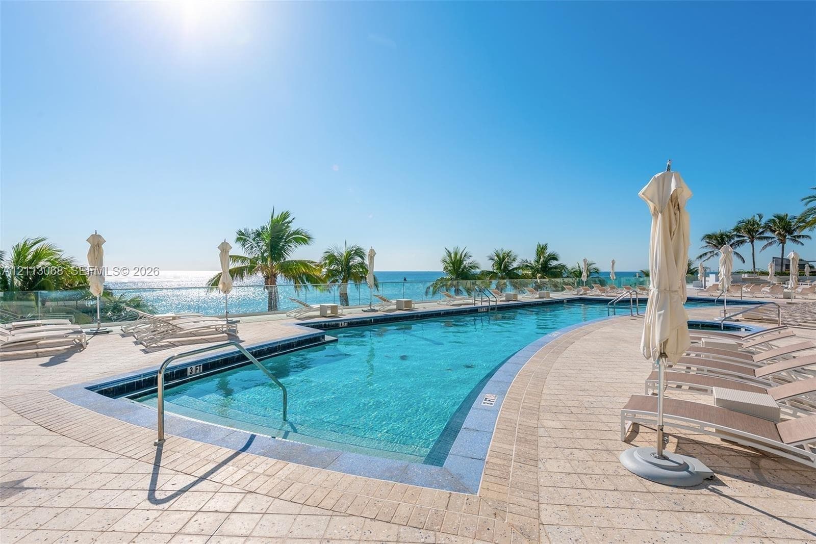 Swimming pool with a stone tile deck, glass safety railing, and integrated spa