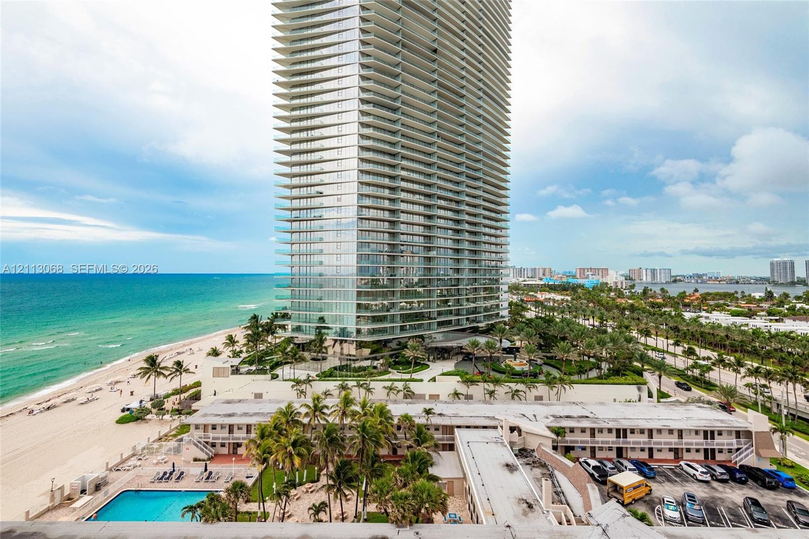 High-rise residential tower featuring floor-to-ceiling glass paneling, wrap-around balconies, an outdoor swimming pool, and direct oceanfront positioning