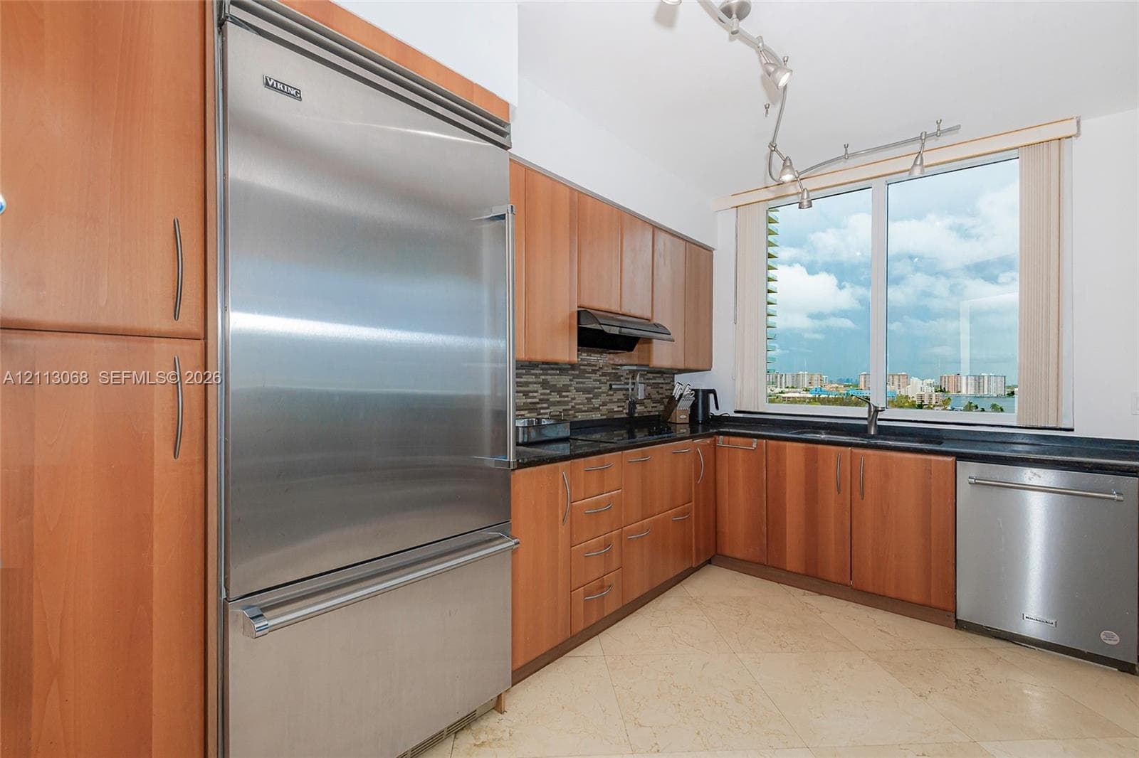 Kitchen featuring wood cabinetry, stainless steel appliances including a professional-grade refrigerator, stone countertops, a mosaic tile backsplash, and overhead track lighting