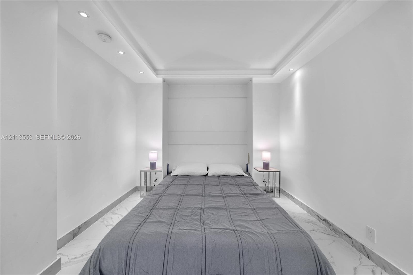 Built-in wall cabinetry, recessed tray ceiling lighting, and polished stone-finish tile flooring