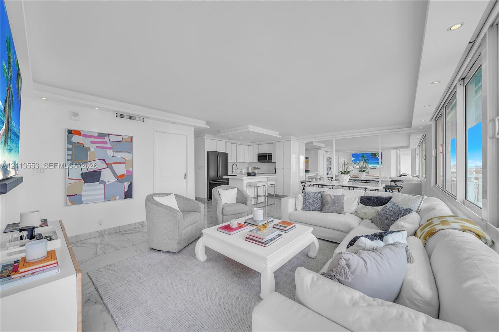 Open-concept interior featuring light-toned stone flooring, recessed ceiling lighting, a kitchen island with stone countertops, and floor-to-ceiling windows