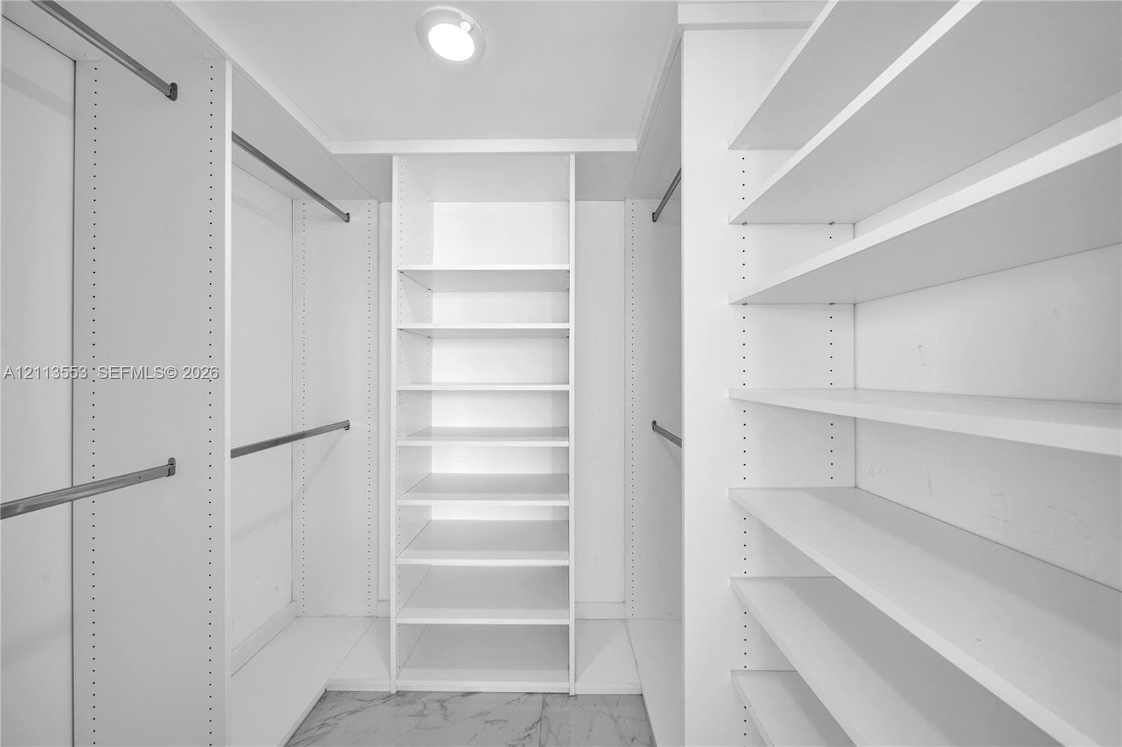Custom walk-in closet featuring white built-in shelving, adjustable storage racks, metal garment rods, and stone-finish flooring