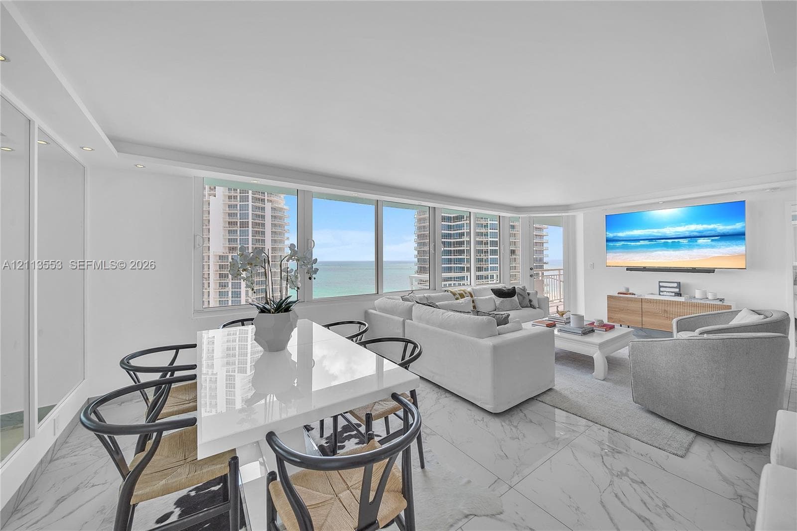 Open-concept living space featuring expansive floor-to-ceiling windows, polished stone-finish flooring, recessed lighting, and wall-mounted media cabinetry