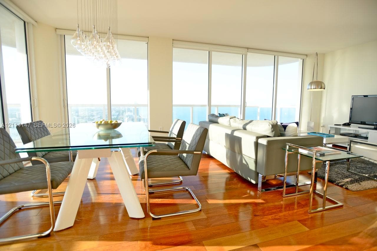 Open-concept interior featuring floor-to-ceiling windows, wood-finish flooring, and a contemporary multi-bulb chandelier