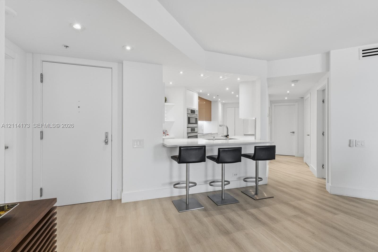 Kitchen featuring a breakfast bar with stone-surfaced countertop, built-in wall oven, recessed lighting, and wood-finish flooring