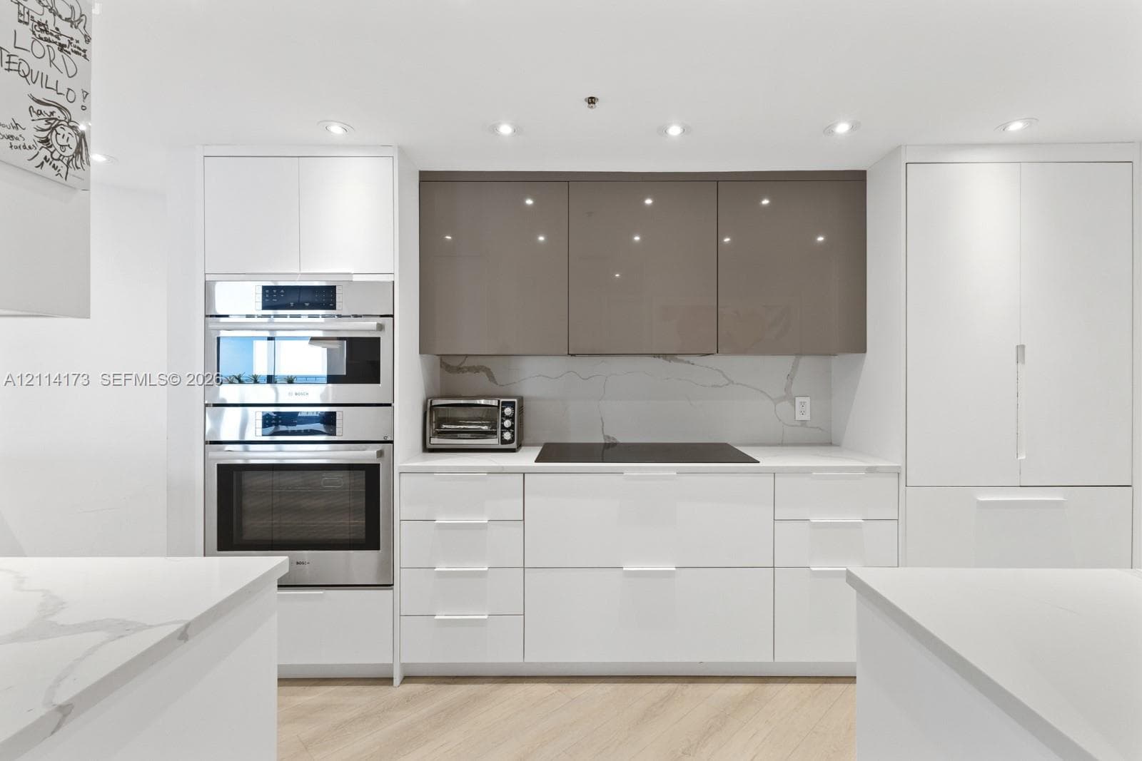Modern kitchen featuring flat-panel high-gloss cabinetry, stone countertops with veining detail, integrated cooktop, built-in stainless steel double ovens, and wood-finish flooring
