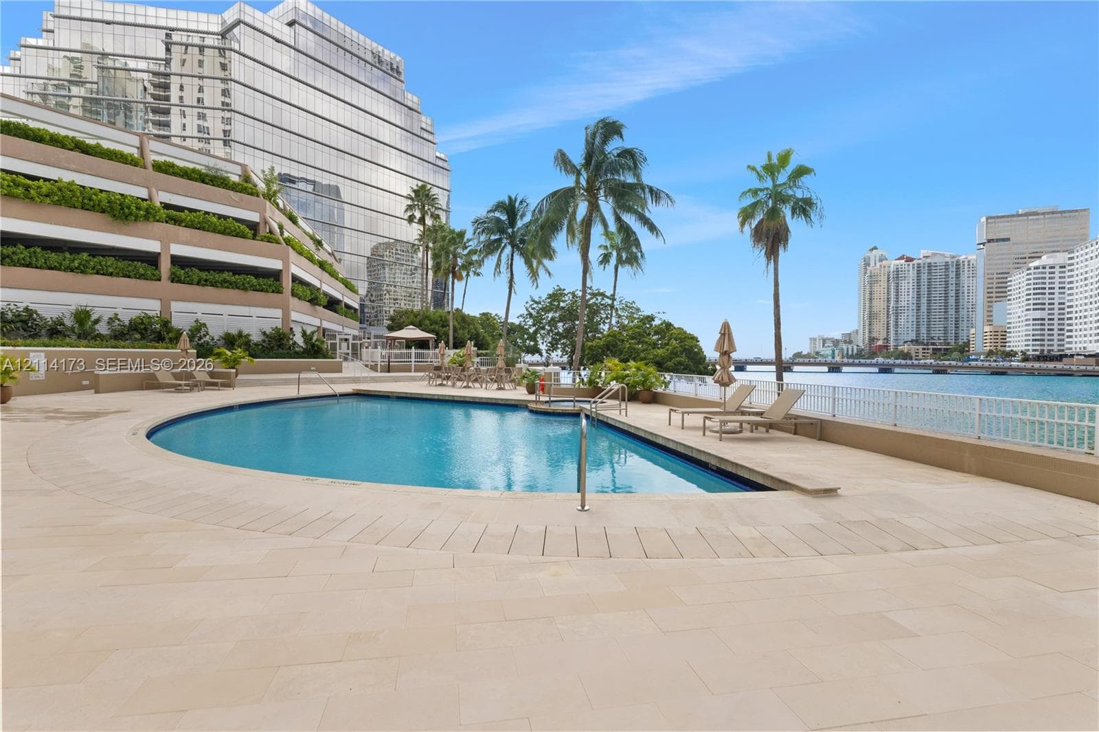 Waterfront swimming pool with stone-tiled deck, integrated spa, and mature palm landscaping