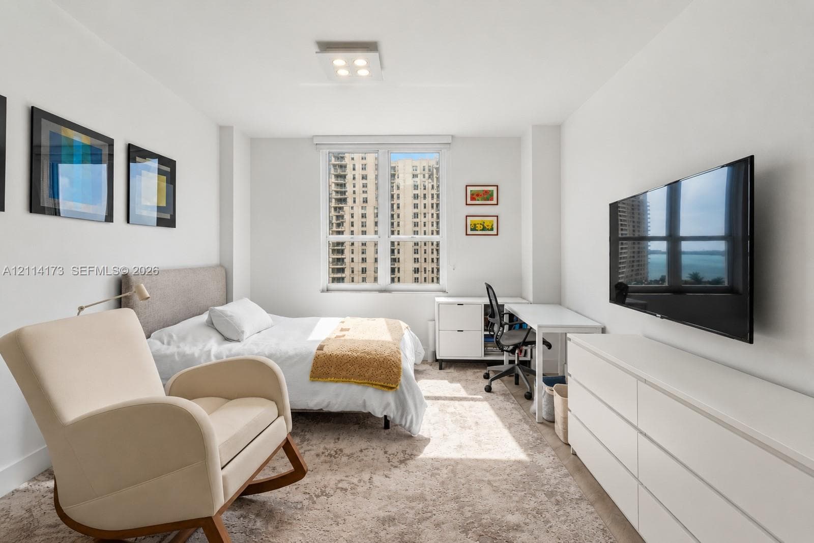 Bright interior space featuring a large window with urban and water scenery, neutral wall finishes, and a modern ceiling-mounted light fixture