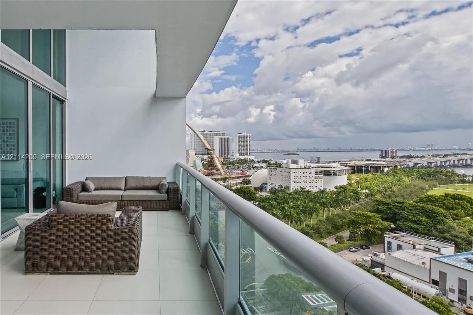Covered balcony with large-format tile flooring, floor-to-ceiling glass sliding doors, and a glass-paneled railing