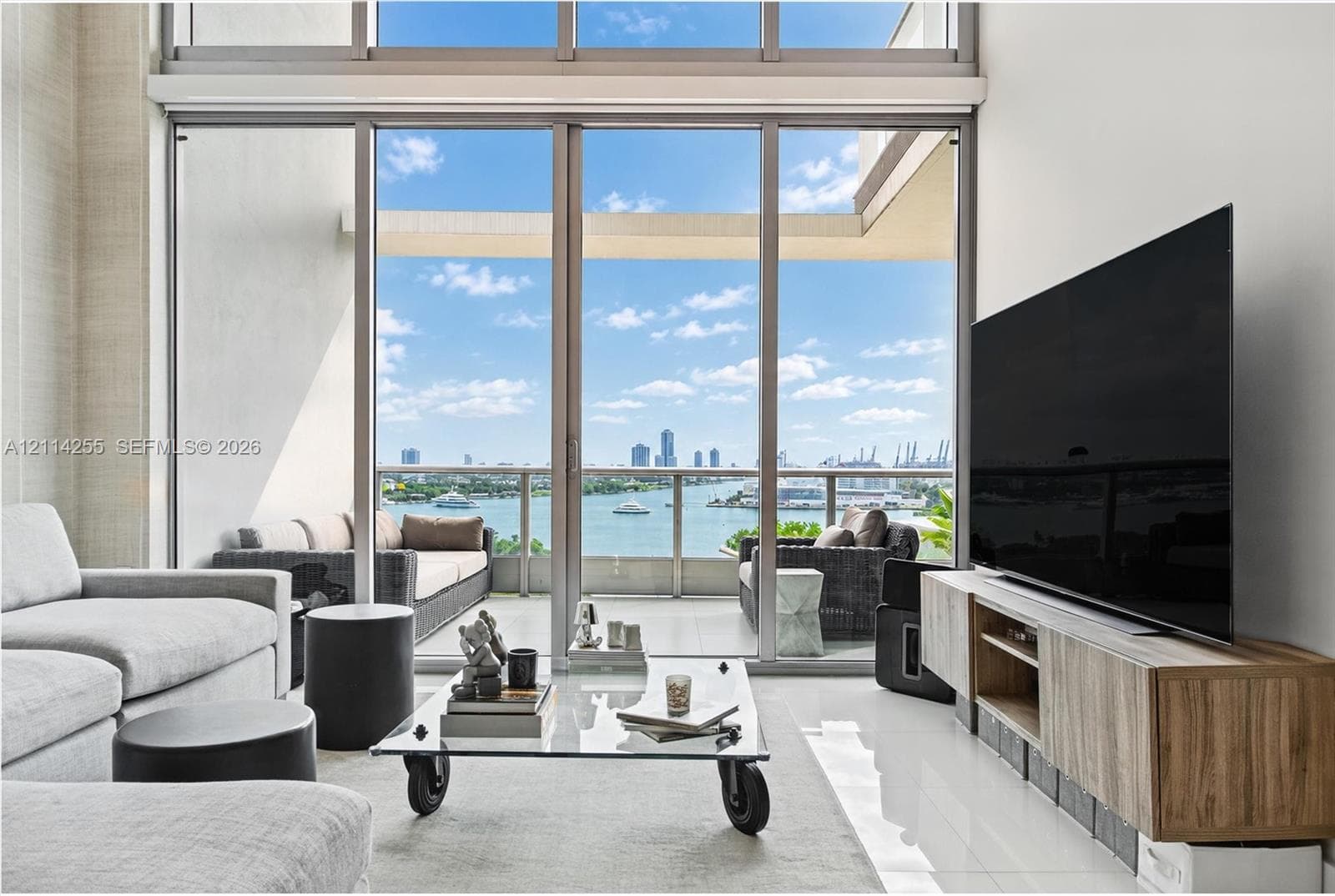 Floor-to-ceiling windows, soaring double-height ceilings, tiled flooring, and a glass-paneled balcony featuring water and cityscape scenery