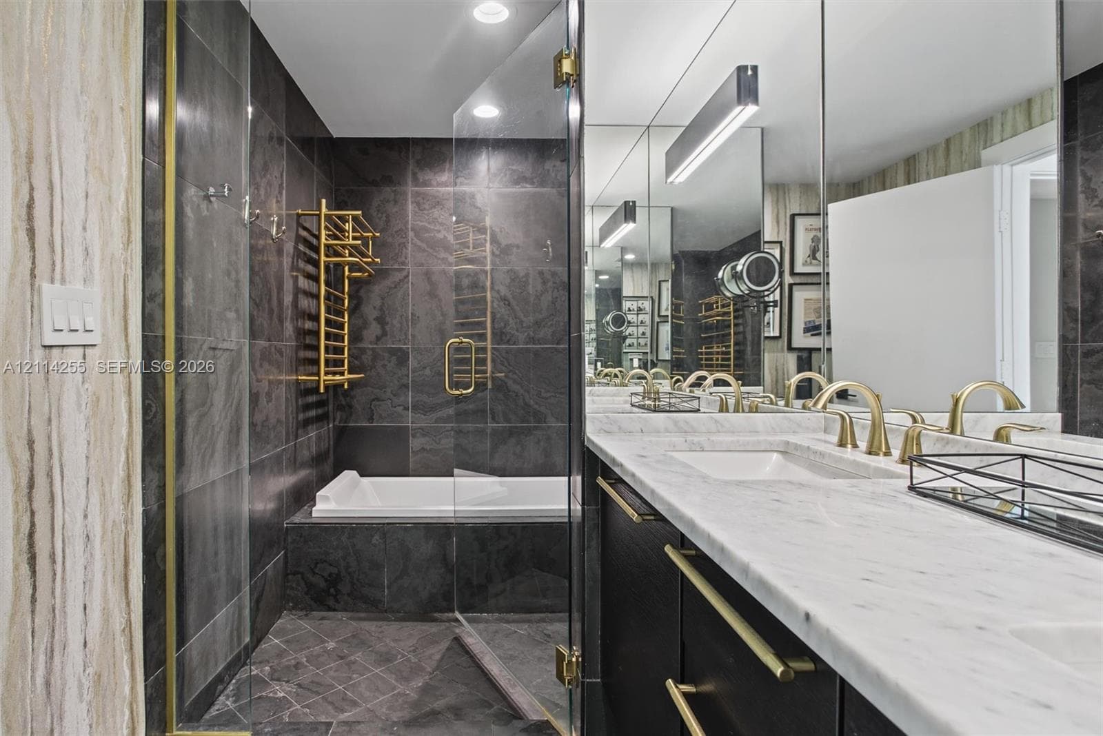 Bathroom featuring a double vanity with stone countertops, dark cabinetry with gold-tone hardware, a glass-enclosed shower, and a built-in tub with wall-mounted gold-tone towel warmer