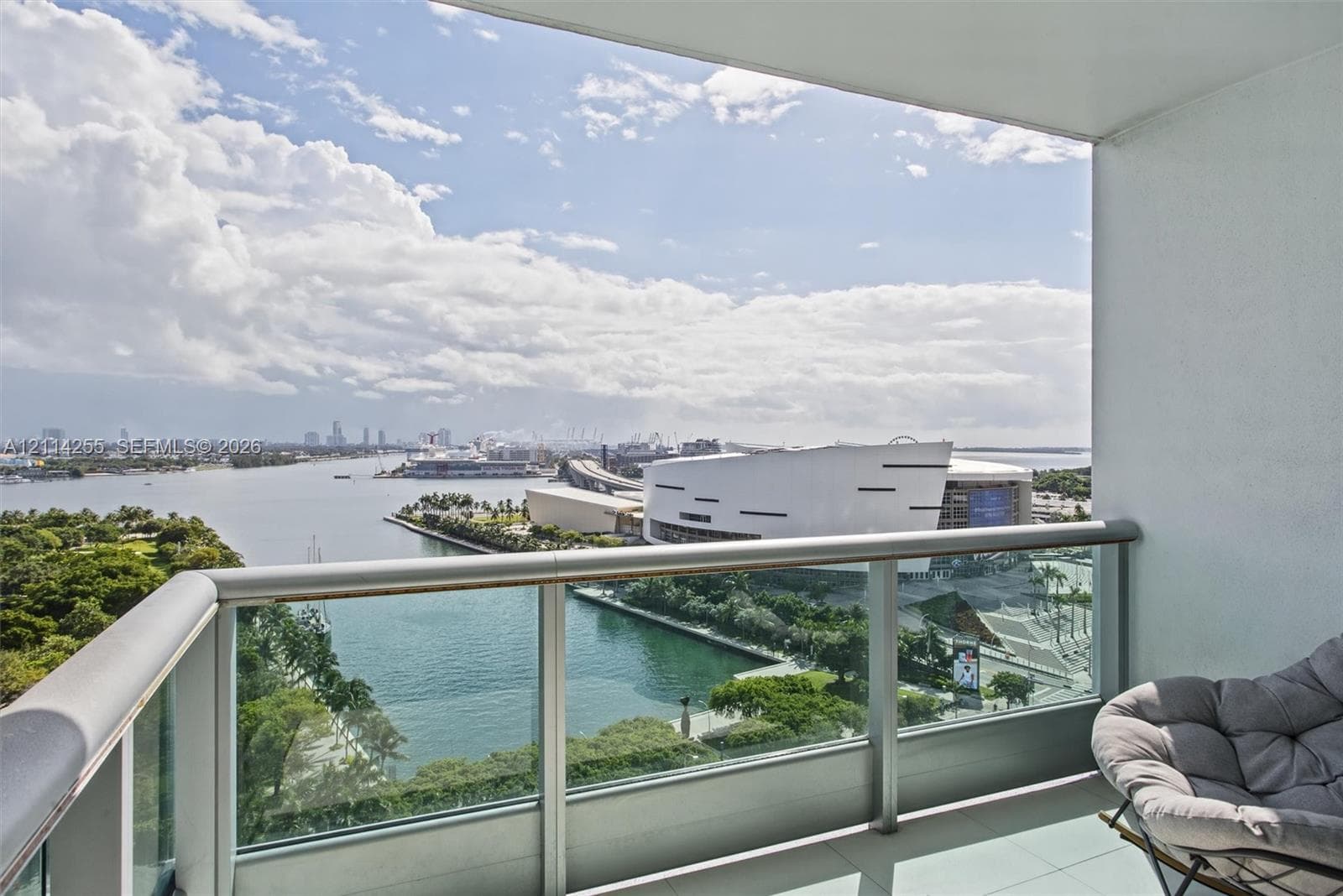 Covered balcony featuring a glass panel railing, metal frame, and tile flooring, oriented toward a water and city skyline horizon