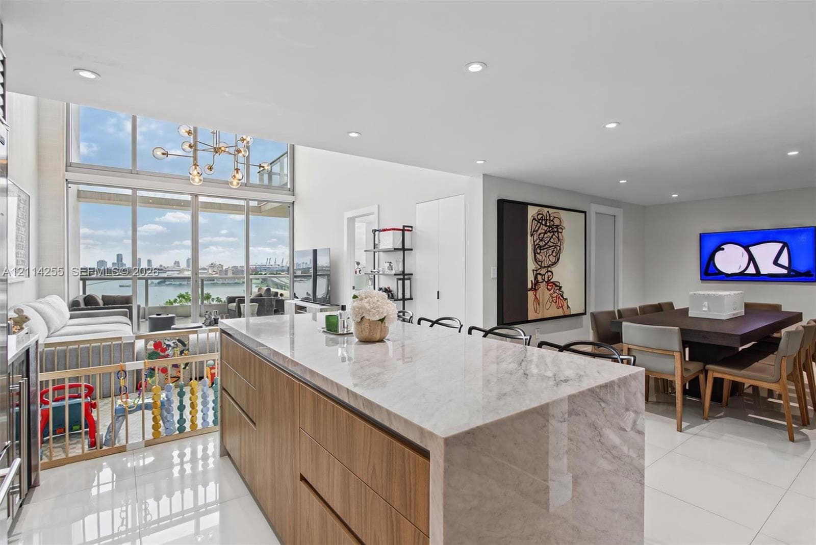 Kitchen island with stone countertop and waterfall edge, flat-panel wood-finish cabinetry, floor-to-ceiling windows, recessed lighting, and large-format tile flooring