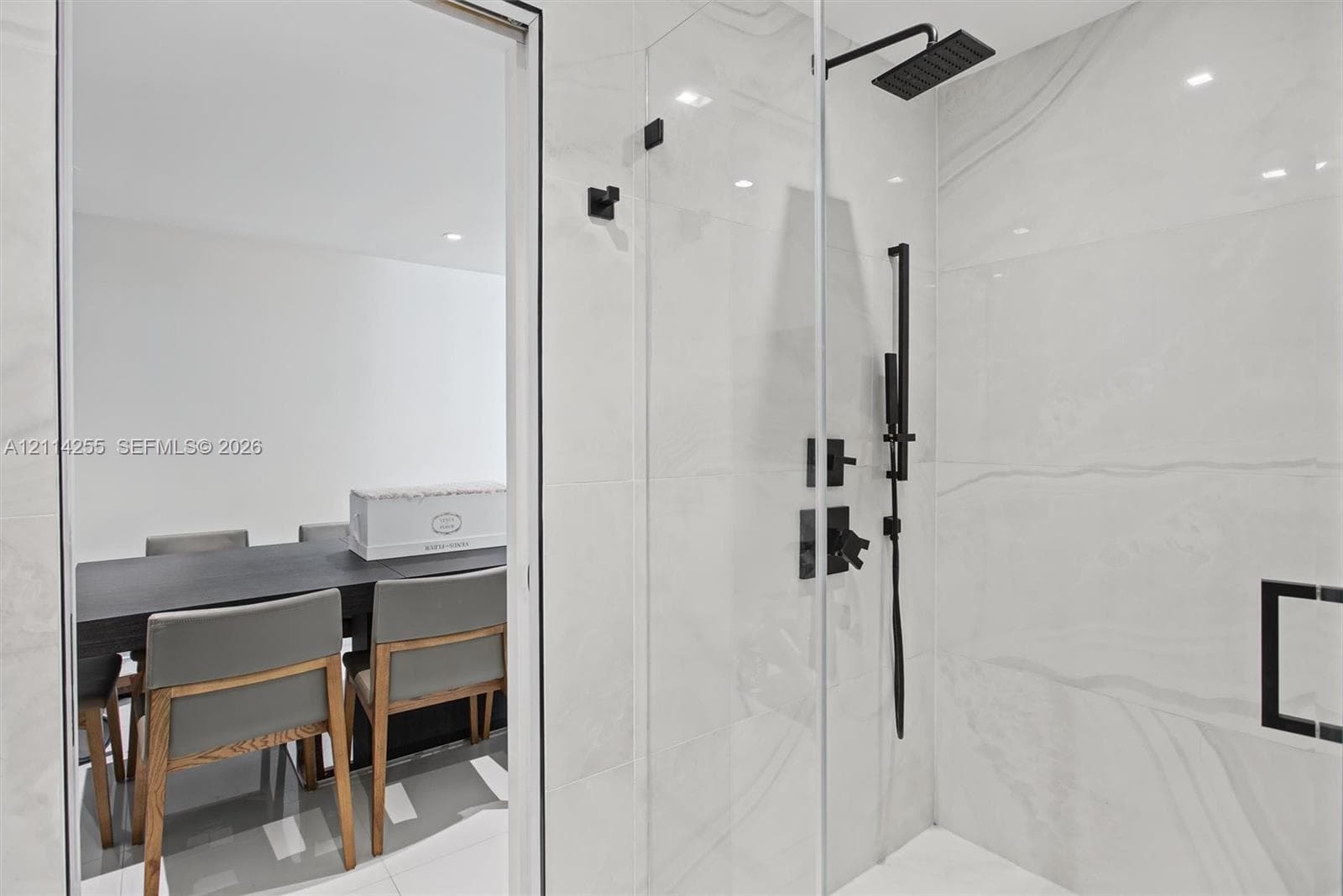 Walk-in shower featuring large-format stone-finish tile, glass enclosure, matte black rainfall showerhead, and matching handheld sprayer