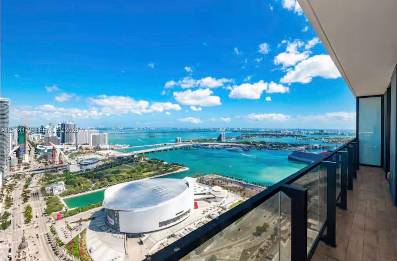 Covered balcony featuring wood-finish flooring and a glass railing with black metal framing, showcasing an expansive waterfront and city skyline panorama